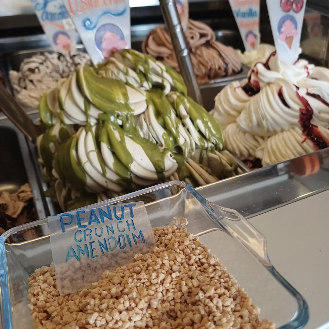 Gelado branco com cobertura verde e gelado de nata com frutos vermelhos; à frente, um tabuleiro de amendoim crocante